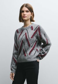 Hall halli kampsun punase, musta ja hõbedase tikandiga siksakmustriga. Omab ümarat kaelust ning pikki varrukad soonikkoes varruka- ja alumiste servadega.