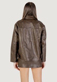 Giacca di pelle marrone con una vestibilità comoda, maniche lunghe e fibbie laterali. Texture liscia con una finitura naturale e dettagli di cucitura minimi.