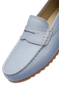 Mocassin en cuir bleu clair avec surpiqûres visibles, bride à languette, et semelle en caoutchouc beige, vu en angle depuis le dessus et le côté.