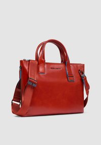 Rote Leder-Tote-Bag mit kurzen Griffen und einem verstellbaren Riemen. Verfügt über blaue Akzente und eine glatte, glänzende Textur.