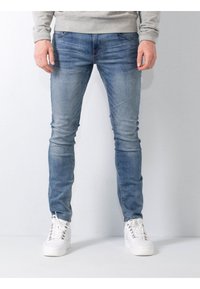 Jeans din denim de culoare albastră deschis, slim-fit, cu un finisaj uzat, buzunare frontale și un design clasic cu cinci buzunare, asortați cu adidași albi.