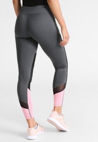 Leggings sportivi grigi con accenti neri, pannelli inferiori rosa e inserti in mesh. Vita alta, forma aderente e materiale dalla texture liscia.