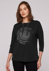 Sudadera negra con mangas 3/4, que presenta un diseño gráfico en texto y puntos plateados. Incluye una capucha con cordón y un corte holgado.