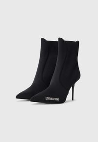 Sorte ankel støvletter laget av glatt stoff, med spiss tå og stiletto-hæl. Logoen "LOVE MOSCHINO" vist i hvitt på siden.