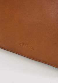 Ruskea teksturoitu nahkalaukku, jossa on kohokuvioitu "s.Oliver" -logo ja näkyvät saumat reunoilla. Tasainen pinta, muotoiltu design.