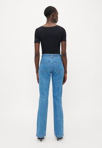 Blå bukseskaft med høy midje og baklommer, kombinert med en svart tettsittende topp. Materialet ser ut som denim med en glatt tekstur.