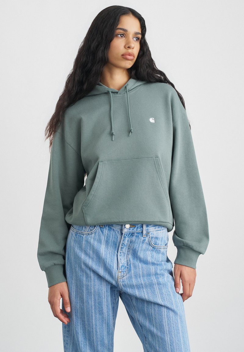 Groene hoodie met voorzak, gemaakt van zachte stof. Draagt met lichtblauwe verticaal gestreepte jeans. Eenvoudig logo op de borst.
