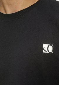 Zwarte katoenen T-shirt met ronde hals, voorzien van een wit merklogo in de linkerbovenhoek. Gladde textuur, korte mouwen.