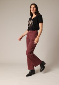 Black V-neck t-shirt with floral heart design, paired with high-waisted burgundy trousers and black heeled ankle boots. Smooth fabric texture.