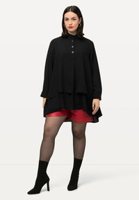 Black layered blouse with a high collar and three front buttons, paired with red satin shorts. Model wears sheer black tights and black heeled boots.