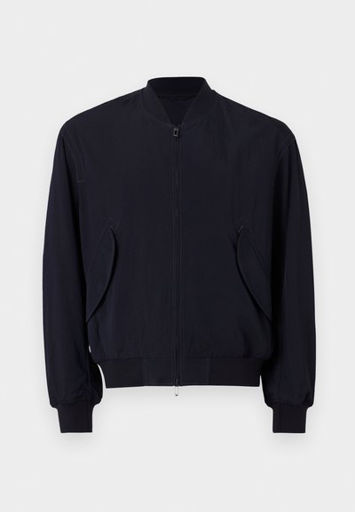 Mornarska bomberska jakna z zadrgo spredaj, rebrastimi manšetami in robom, ki ima kotno žepno odprtino in gladko, lahko tkanino.