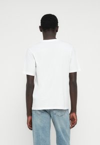 Valkoinen puuvillainen t-paita, jossa on lyhyet hihat ja pyöreä pääntie, esitettynä takaapäin, yhdistettynä vaaleansinisiin farkkuihin.