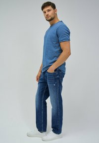 T-shirt à rayures bleues à manches courtes associé à un jean en denim bleu délavé et des baskets blanches, offrant une coupe décontractée et des poches latérales.