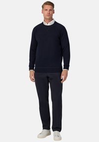 Jūrinės spalvos megztinis su apvalia iškirpte, įrištais rankogaliais ir apatine dalimi. Sukombinuotas su tamsiomis kelnėmis ir šviesiomis sportbačiais.