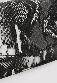 Clutch en estampado de serpiente en blanco y negro con una superficie de cuero texturizado, que presenta un diseño angular y un solapa plegable para el cierre.