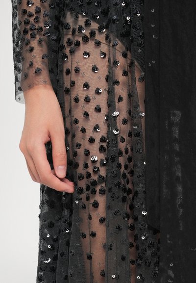 Käsi resting koos läbipaistva musta kangaga, mis on kaetud väikeste mustade sädelustega heledal taustal.