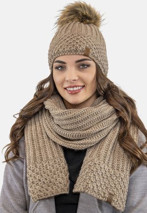 Beanie in lana color beige con pompon in pelliccia sintetica e sciarpa coordinata a trama texturizzata, caratterizzata da motivi spessi e intrecciati in un design casual.