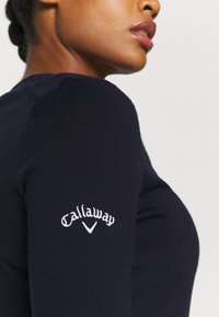 Mornarica pletena majica s prilagođenim dizajnom i rebrastom teksturom. Izvezeni "Callaway" logo u bijeloj boji na lijevoj rukavu.