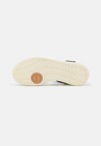 Zapatilla navy con suela de goma texturizada; cuenta con surcos para tracción y un logotipo circular de madera en el talón, proporcionando agarre y estabilidad.