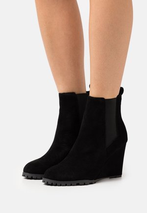 Bottines à talons compensés en daim noir avec des panneaux latéraux en élasthanne et une semelle extérieure en caoutchouc texturé ; finition lisse et design à orteil effilé.