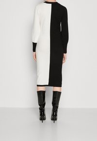 Stickad klänning med delad design i svart och vitt, långa puffärmar och längd till mitten av vadmåttet. Matchad med blanka svarta knähöga stövlar.