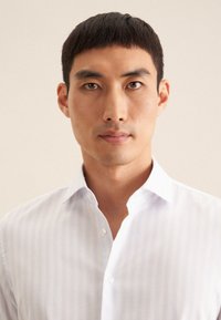 Weißes Hemd mit hellblauen vertikalen Streifen, Knopfleiste und weiter Kragen. Glatte Textur mit einer taillierten Passform.