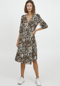 Ziedu raksta kleita ar V veida kakla izgriezumu, trim stundu piedurknēm un izteiktu jostas vietu. Tajā ir zemes toņu zaļumi, brūni un balti akcenti. Kopā ar baltām sporta kedām.