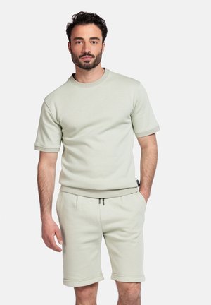 Lichtgroen sweatshirt met korte mouwen en ronde hals, gecombineerd met bijpassende knielange shorts. De stof lijkt zacht met omgeslagen mouwen en zoomdetails.