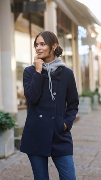 Marineblauer Wollmantel mit doppelt geknöpftem Verschluss und zwei Fronttaschen, über einem grauen Kapuzenpullover getragen. Jeans aus Denim runden das Outfit ab.