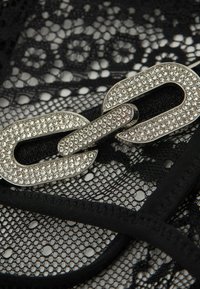Tissu en dentelle noire avec un accent de chaîne argentée ornée de diamants, mettant en valeur des motifs complexes et une texture douce.