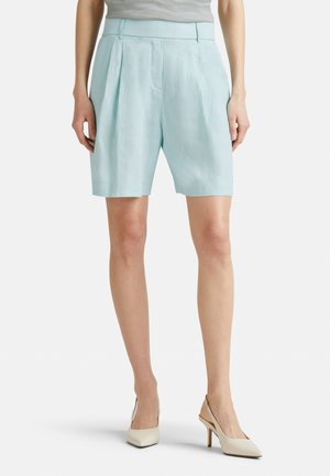Shorts en lin bleu clair avec des plis, longueur mi-cuisse, et une taille plate. Associés à des talons aiguilles pointus blancs cassés.
