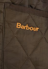 Gepolstertes braunes Gewebe mit Rautenmuster; verfügt über ein orangefarbenes gesticktes "Barbour"-Logo; strukturierte Oberfläche und sichtbare Nähte.