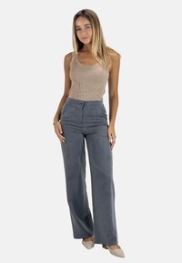 Débardeur côtelé beige clair associé à un pantalon gris taille haute et large avec un bouton sur le devant et une texture lisse. Chaussures de couleur neutre.