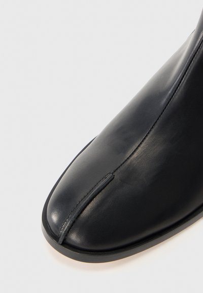 Stivale alla caviglia in pelle nera con un design elegante, punta arrotondata, cuciture visibili e una texture liscia, caratterizzato da una silhouette minimalista.