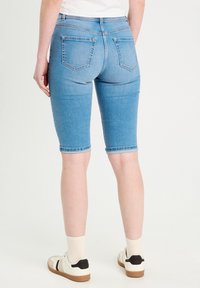 Bermuda en denim de couleur bleu clair, longueur genou, avec une coupe ajustée. Les caractéristiques comprennent un design classique à cinq poches et des coutures ton sur ton.