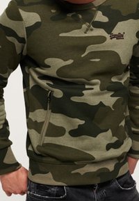 Maskáčová mikina v zelené a khaki barvě, s kapsou na zip na levé straně, kulatým výstřihem a žebrovanými manžetami.