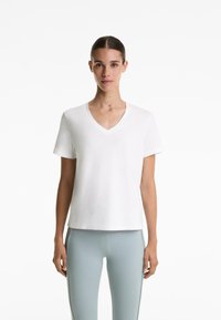 Tricou alb din bumbac, cu mânecă scurtă și decolteu în V, având o croială lejeră și o textură fină. Poartă-l cu leggings ușor albaștri.
