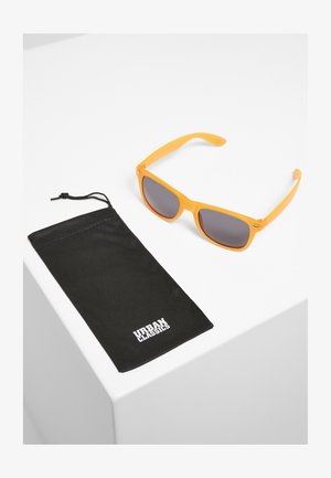 Ochelari de soare din plastic portocalii cu lentile închise, alături de o punguță moale neagră, imprimată cu "URBAN CLASSICS" în alb pe față.