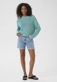 Pullover blu chiaro lavorato a maglia con una vestibilità ampia e un motivo a texture, abbinato a shorts in denim con orlo arrotolato e sandali neri a pochette.