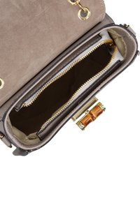 Interno di una borsa in suede marrone con una fodera beige, caratterizzata da cerniere dorate, un gancio dorato e un accento in legno sul gancio.