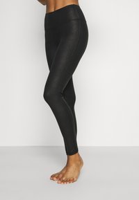 Leggings neri con una vita alta, realizzati in un materiale liscio e leggermente lucido. Design aderente senza motivi o accessori visibili.