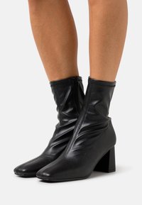 Bottines noires en simili cuir avec un bout effilé, un haut décontracté et un talon bloc, dotées d'une fermeture éclair sur le côté.