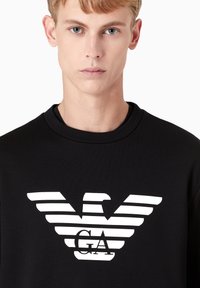 Felpa nera con logo di un aquila a strisce bianche sovrapposto alla scritta "GA". Tessuto morbido e scollatura tonda, design minimalista.