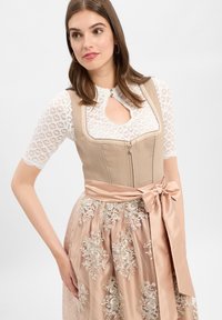 Beiges Mieder mit Reißverschluss, weiße Spitzenbluse mit kurzen Ärmeln und ein rosa Rock mit Blumenstickerei sowie einer gebundenen Satin-Gürtelschleife.