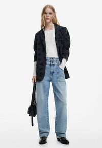 Blazer noir avec motif floral, top blanc à encolure dégagée, jean léger oversize bleu clair et sac à main noir. Textures lisses et coupe décontractée.