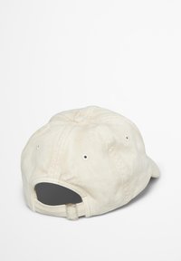 Crèmekleurige pet met een ronde kroon, textuur van stof, gestikte details en een verstelbare metalen gesp aan de achterkant.