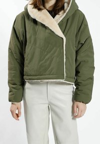 Grön kort puffjacka med en mjuk krämfärgad fuskpälskrage. Har diagonalt quiltad textur och elastiska ärmslut.