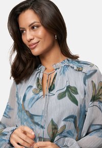 Floral print blouse with blue and green leaves on a striped light background. Features a gathered neckline and puffed sleeves with ruffled cuffs.