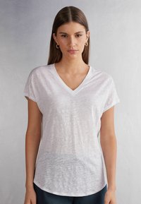 T-shirt bianco con scollatura a V, maniche corte, tessuto morbido e leggero, texture leggermente trasparente e orlo curvo.