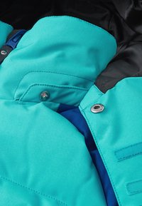 Teal-Farbenes Puffer-Jackett mit hohem Kragen, metallischen Druckknöpfen und kontrastierender blauer Futter. Glattes, strapazierfähiges Material mit gesteppten Details.